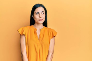 Güzel, genç bir kadın, günlük kıyafetler giymiş, gülümsüyor, yan tarafa bakıyor ve düşünüyor.. 