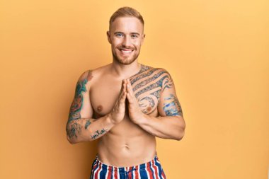 Mayo giyen, elleri bağlı dua eden, kendinden emin gülümseyen beyaz bir genç.. 