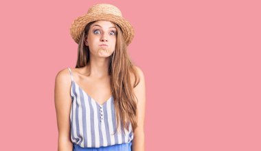 Yazlık şapkalı güzel sarışın kadın komik yüzlü yanakları şişiriyor. Havayla şişmiş ağız, çılgın bir ifade.. 