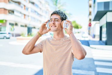 Genç, yakışıklı, beyaz, gülümseyen, müzik dinleyen, kulaklık takan, şehirde yürüyen bir adam..