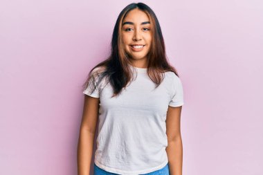 Yüzünde mutlu ve havalı bir gülümseme olan gündelik beyaz tişört giyen genç Latin kadın. şanslı kişi. 