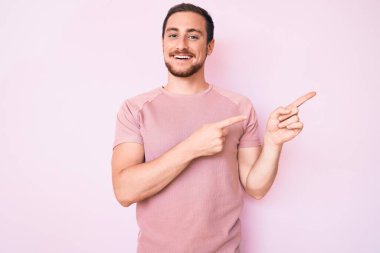 Gündelik tişört giyen genç yakışıklı adam gülümseyip kameraya bakıyor ve iki eliyle ve parmaklarıyla kenarı işaret ediyor.. 