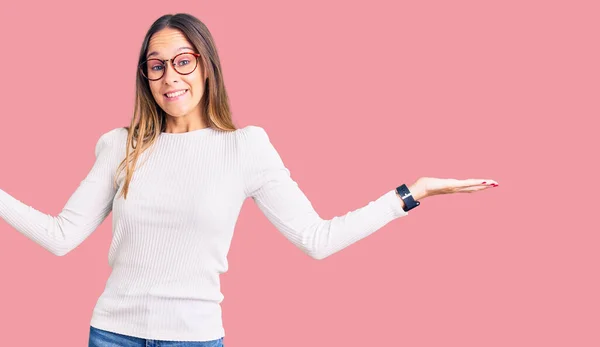 カジュアルな白いセーターと眼鏡を身に着けている美しいブルネットの若い女性は 腕や手を上げて混乱した表情 疑わしい概念 — ストック写真