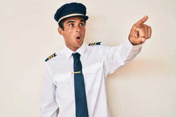 Junger Hispanischer Mann Flugzeugpilotenuniform Zeigt Überrascht Mit Dem Finger Voraus — Stockfoto
