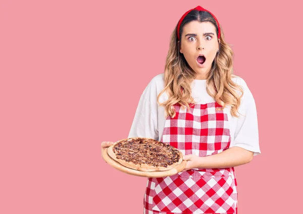 Ung Kaukasiska Kvinna Bär Förkläde Håller Pizza Rädd Och Förvånad — Stockfoto