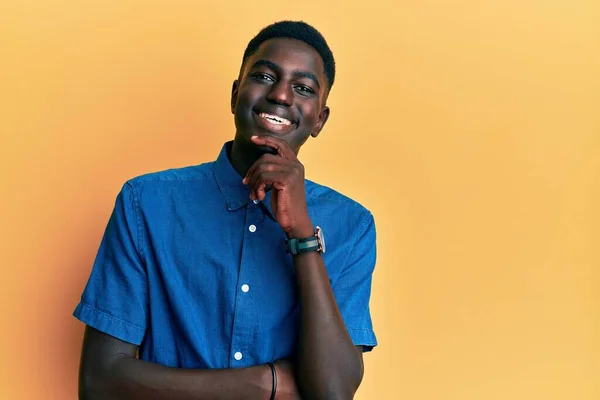 カジュアルな服を着た若いアフリカ系アメリカ人男性は カメラに自信を持って笑顔で交差腕と顎の手で見ています ポジティブな — ストック写真