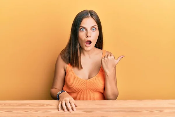 Young Caucasian Woman Wearing Casual Clothes Sitting Table Surprised Pointing — Stock Photo, Image