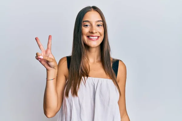 勝利サインをしているカメラには幸せそうな顔をして笑顔でカジュアルな服を着ている若いヒスパニック系の女性 — ストック写真