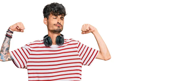 腕の筋肉を示すヘッドフォンを使用して音楽を聞いている若いヒスパニック系の男は誇りに思って笑っている フィットネスのコンセプト — ストック写真