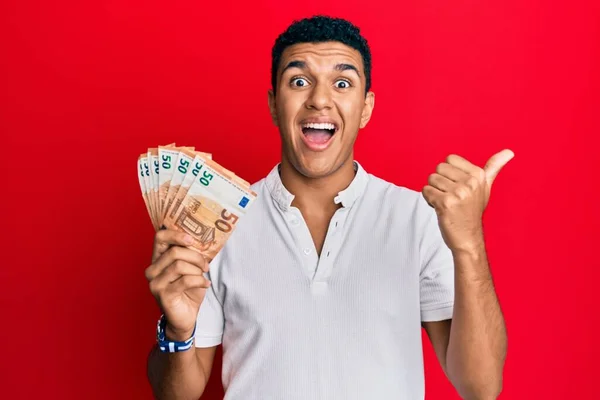 Young Arab Man Holding Euro Banknotes Pointing Thumb Side Smiling — Stock Photo, Image