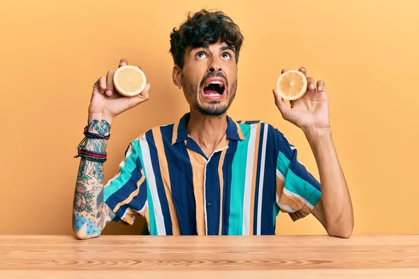 Young Hispanic Man Sitting Table Holding Lemon Angry Mad Screaming — Stok fotoğraf