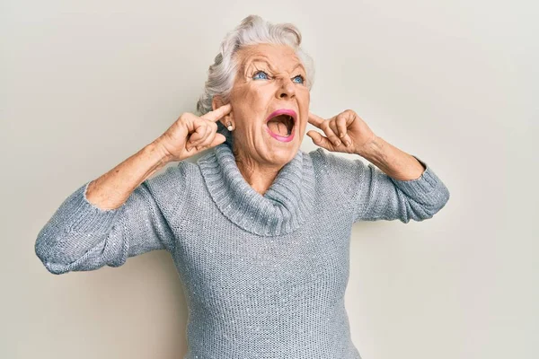 Senior grey-haired woman covering ears with finger angry and mad screaming frustrated and furious, shouting with anger. rage and aggressive concept.