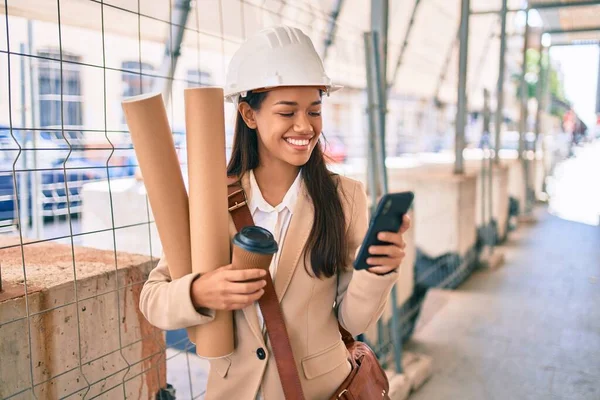 市内で設計図を保持し スマートフォンを使用して若いラテン語の建築家の女の子 — ストック写真