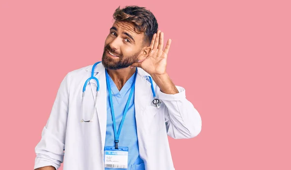 医師の制服を着た若いヒスパニック系の男性と 噂やゴシップに耳を傾ける耳の上に手で笑みを浮かべて聴診器 聴覚障害の概念 — ストック写真