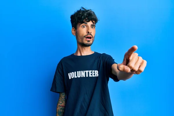 若いヒスパニック系の男がボランティアTシャツを指で指して身に着けている前に驚いて 口を開けて驚くような表現は 前に何か — ストック写真