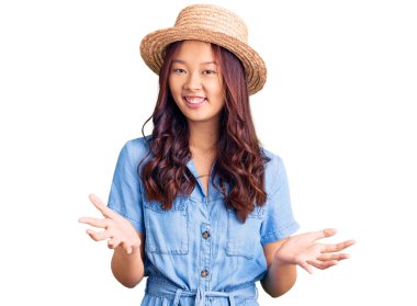 Genç ve güzel Çinli kız yaz şapkası takıyor. Neşeli gülümsüyor. Kollarını açıp dostça karşılıyor. 