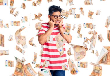 Yakışıklı Latin Amerikalı genç adam gündelik kıyafetler ve gözlük takıyor kulakları parmaklarıyla kapatıyor yüksek sesli müzik sesi için rahatsız edici ifadeleri var. sağır kavramı.