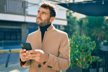 Zarif ceketli yakışıklı bir iş adamı. Açık havada akıllı telefon kullanıyor.
