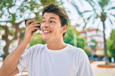 Kafkasyalı genç adam gülümsüyor. Şehirdeki akıllı telefonu kullanarak mutlu bir şekilde sesli mesaj dinliyor..