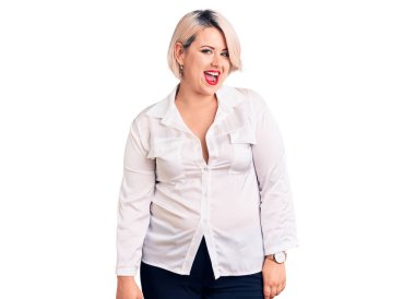 Genç sarışın ve cüsseli bir kadın. Günlük gömlek giyiyor. Kameraya seksi bir ifadeyle bakıyor, neşeli ve mutlu bir yüz ifadesi var.. 