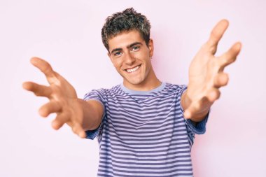 Sıradan kıyafetler giymiş genç yakışıklı bir adam kameraya bakıyor ve sarılmak için kollarını açmış gülümsüyor. Mutluluğu kucaklayan neşeli bir ifade.. 