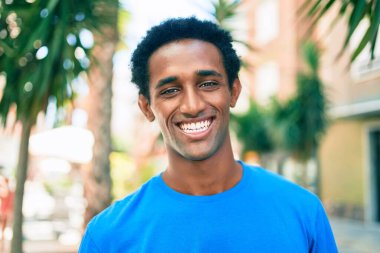 Yakışıklı siyah Afrikalı adam dışarıda mutlu gülümsüyor.