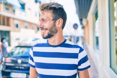 Sakallı yakışıklı beyaz adam dışarıda mutlu bir şekilde gülümsüyor. Akıllı telefon kullanıyor.