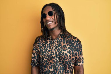 Örgü örgülü, hayvan desenli tişörtlü, güneş gözlüklü yüzünde mutlu ve havalı bir gülümseme olan Afro-Amerikan bir adam. şanslı kişi. 