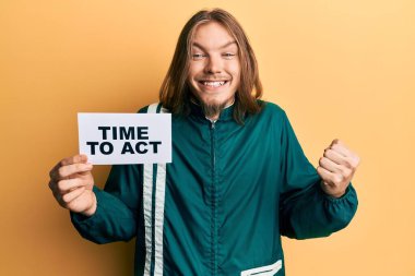 Uzun saçlı yakışıklı beyaz adam bayrak sallıyor gururla haykırıyor, zaferi kutluyor ve başarıyı kollarını kaldırarak kutluyor. 