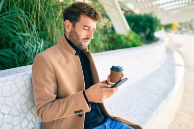 Zarif ceketli yakışıklı bir iş adamı. Açık havada akıllı telefon kullanıyor.