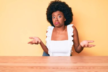 Sıradan kıyafetler giyen, kafası karışmış, elleri ve kolları havada genç bir Afrikalı Amerikalı kadın. şüphe kavramı. 