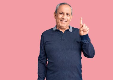 Kıdemli yakışıklı adam gündelik polo giyip bir numaralı parmağını gösterirken kendinden emin ve mutlu bir şekilde gülümsüyor.. 