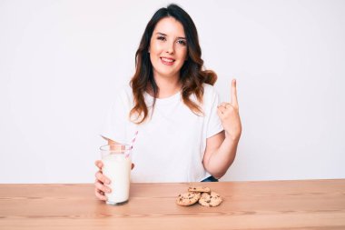 Genç, güzel esmer kadın bir bardak taze süt ve kurabiyelerle gülümseyen bir fikir ya da soru işareti ile gülümseyen mutlu yüzlü, bir numara. 