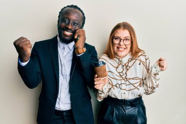 Genç ırklar arası bir çift akıllı telefon kullanıyor ve bir fincan kahve içiyor gururla haykırıyor, zaferi kutluyor ve kollarını kaldırarak başarıyı kutluyor. 