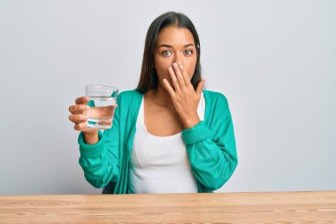 Güzel İspanyol kadın bir bardak su içerek ağzını eliyle kapadı, şok oldu ve hata yapmaktan korktu. şaşırmış ifade 