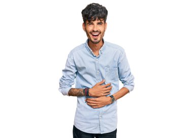 Gündelik kıyafetler giyen genç İspanyol adam gülümseyerek kahkahalarla gülüyor çünkü elleri vücutta olan komik, çılgın bir şaka.. 