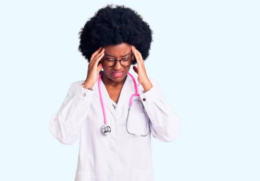 Genç Afro-Amerikalı kadın doktor önlüğü giyiyor ve steteskop kullanıyor. Başı ağrıyor çünkü stres altında. migren ağrısı. 
