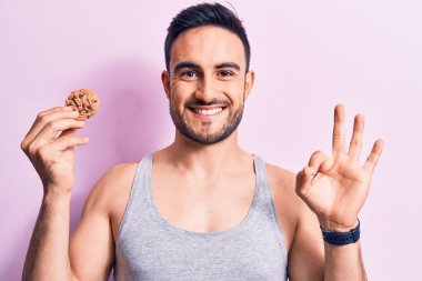 Sakallı, kolsuz tişörtlü, çikolatalı kurabiye yiyen, parmaklarıyla imza atan, güler yüzlü, dost canlısı, mükemmel bir sembol olan genç yakışıklı bir adam.