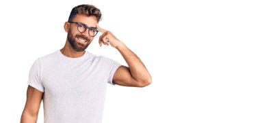 Gündelik kıyafetler ve gözlük takan genç İspanyol bir adam tek parmakla kafasını işaret ediyor, harika bir fikir ya da düşünce, iyi bir hafıza. 