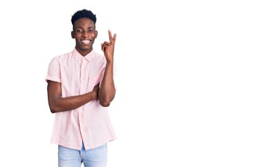 Genç Afro-Amerikalı sıradan kıyafetler giyen, gülen yüzlü, kameraya göz kırpan zafer işareti yapan genç bir adam. İki numara.. 