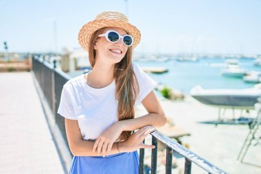 Genç sarışın kadın tatilde mutlu bir şekilde gülümsüyor. Kentin caddesinde korkuluklara yaslanıyor.