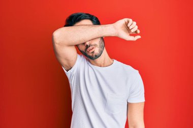 Latin kökenli genç bir adam, sıradan beyaz tişörtler giyip gözlerini kollarıyla kapatıyor, ciddi ve üzgün görünüyor. Görme, saklama ve reddetme konsepti 