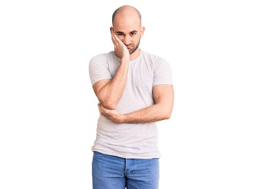 Genç, yakışıklı, rahat tişört giyen, yorgun ve bunalımdan sıkılmış görünen, kollarını kavuşturan bir adam.. 