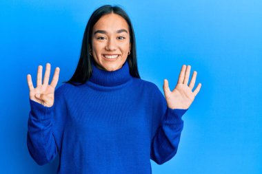 Genç Asyalı kadın günlük kışlık süveter giyer ve dokuz numaralı parmaklarıyla gülümseyerek mutlu ve kendinden emin bir şekilde onu işaret eder.. 