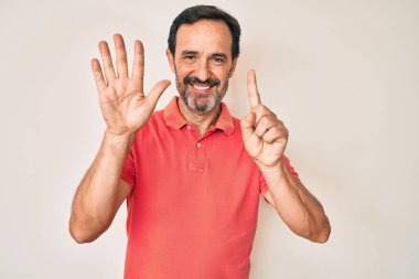 Orta yaşlı İspanyol bir adam gündelik giysiler giyip altı numaralı parmaklarıyla işaret ederken kendinden emin ve mutlu gülümsüyor.. 