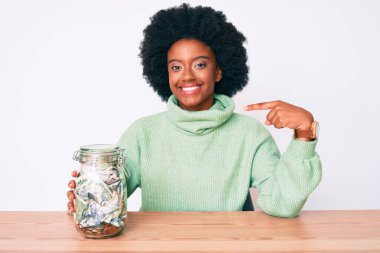 Genç Afro-Amerikalı kadın elinde kavanozla kendini mutlu ve gururlu olarak gösteren birini işaret ediyor. 