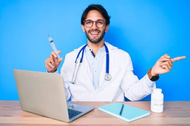 Klinikteki yakışıklı İspanyol doktor elinde şırıngayla gülümsüyor. 