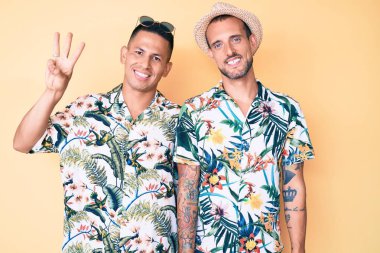 Yaz şapkası takan ve Hawaii gömleği giyen iki genç gay üç numarayı gösterip gösterirken kendinden emin ve mutlu bir şekilde gülümsüyor.. 