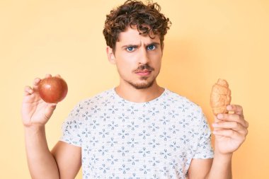 Kıvırcık saçlı, elma tutan, kruvasan kuşkucu ve gergin genç beyaz bir adam sorun yüzünden üzgün. negatif kişi. 