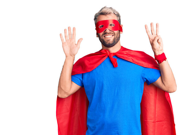 Young blond man wearing super hero custome showing and pointing up with fingers number eight while smiling confident and happy. 